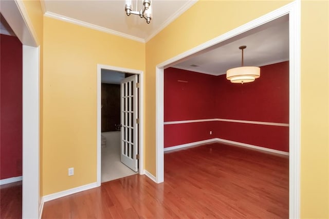 empty room featuring an inviting chandelier, wood-type flooring, and crown molding