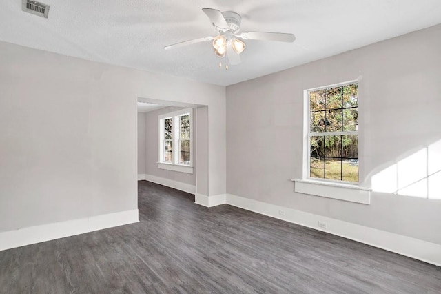 empty room featuring dark wood-type flooring, ceiling fan, and a healthy amount of sunlight