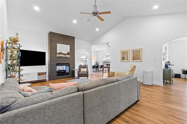 living room with a large fireplace, ceiling fan, high vaulted ceiling, and light hardwood / wood-style flooring