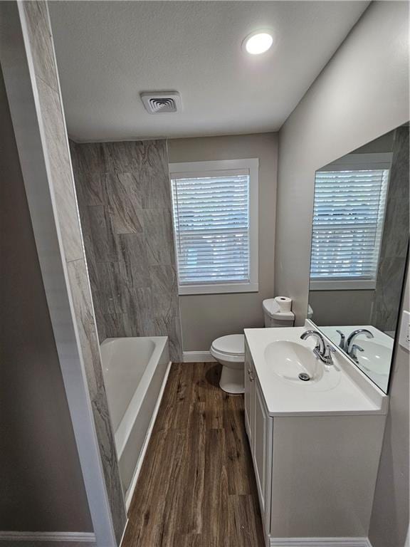 full bathroom with hardwood / wood-style flooring, vanity, tiled shower / bath combo, toilet, and a textured ceiling