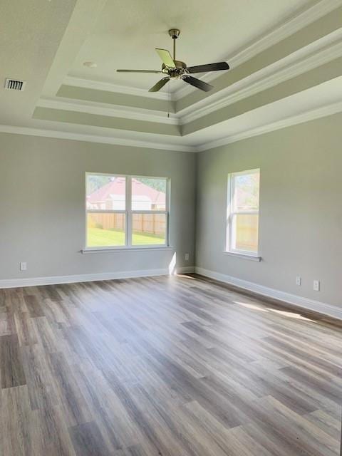 empty room featuring crown molding, ceiling fan, wood-type flooring, and a tray ceiling