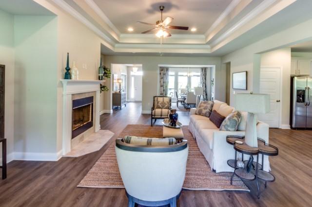 living room with ceiling fan, a high end fireplace, a raised ceiling, crown molding, and dark wood-type flooring