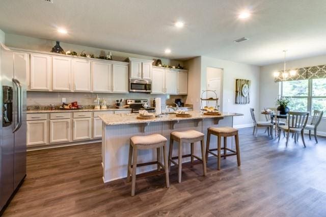 kitchen with stainless steel appliances, decorative light fixtures, a center island with sink, and white cabinets