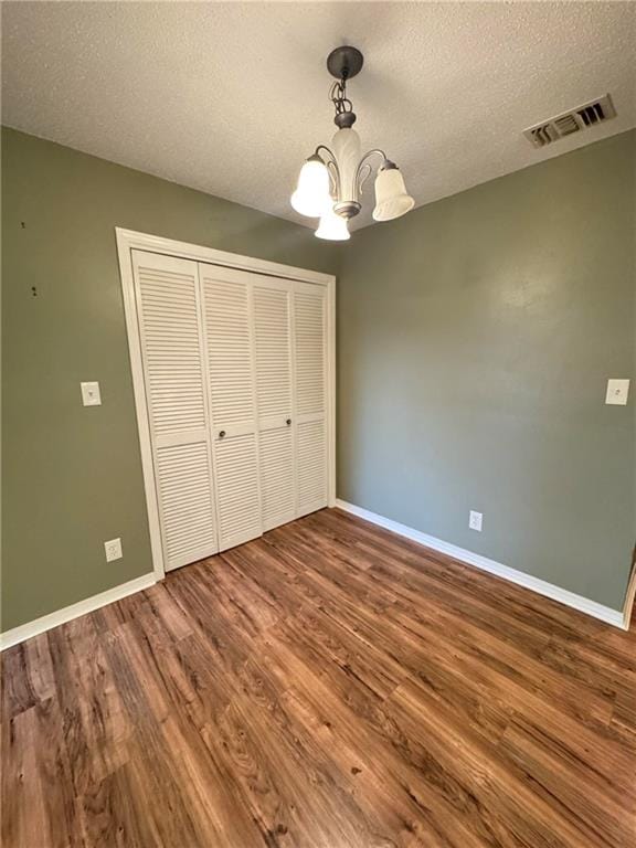 unfurnished bedroom featuring an inviting chandelier, a textured ceiling, and hardwood / wood-style floors