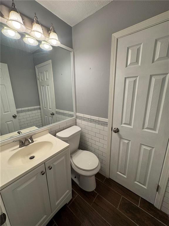 bathroom with toilet, tile walls, vanity, and a textured ceiling