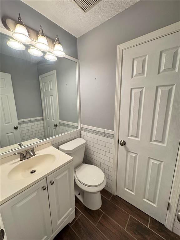 bathroom featuring toilet, tile walls, vanity, and a textured ceiling