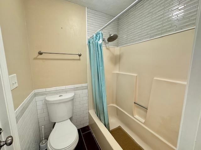 bathroom featuring tile walls, toilet, and shower / bathtub combination with curtain