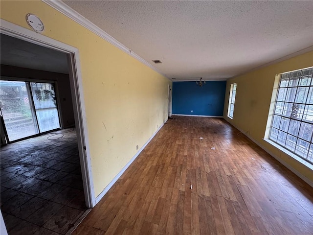 unfurnished room featuring ornamental molding, a textured ceiling, an inviting chandelier, and dark hardwood / wood-style flooring