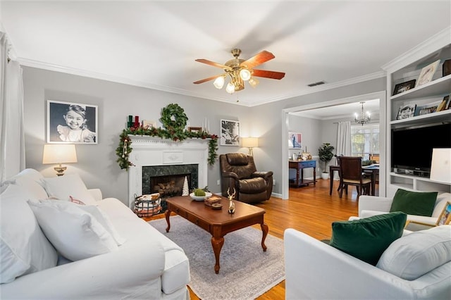 living room with ceiling fan with notable chandelier, a high end fireplace, ornamental molding, and hardwood / wood-style floors