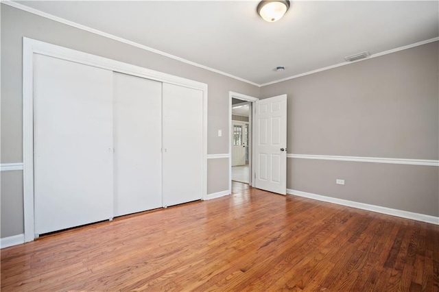 unfurnished bedroom featuring baseboards, wood finished floors, visible vents, and crown molding