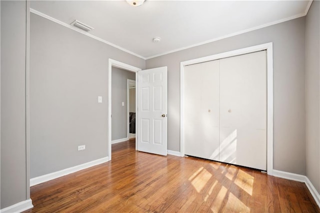 unfurnished bedroom featuring wood finished floors, visible vents, baseboards, ornamental molding, and a closet