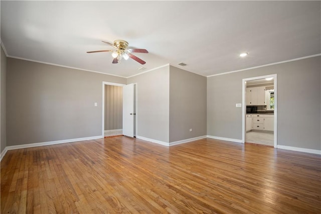 empty room featuring light wood finished floors, baseboards, visible vents, and ornamental molding