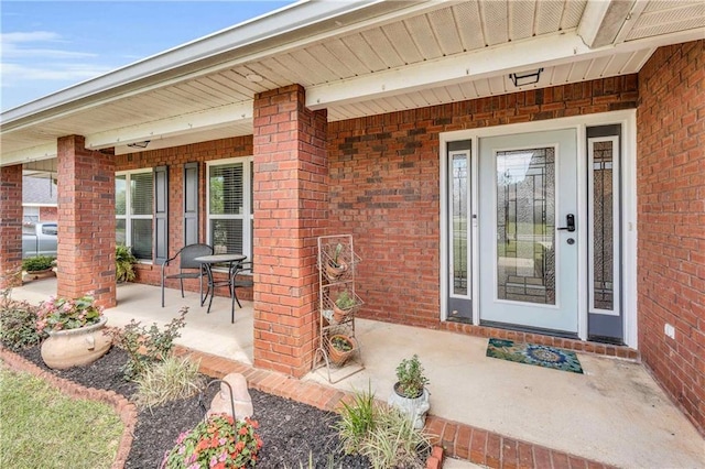 view of exterior entry with brick siding and a porch