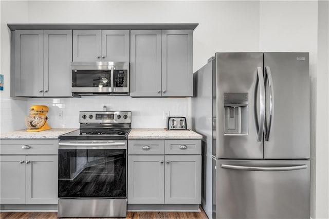 kitchen featuring light stone countertops, gray cabinets, backsplash, and stainless steel appliances