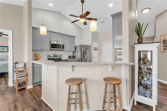 kitchen featuring dark wood finished floors, ceiling fan, gray cabinetry, appliances with stainless steel finishes, and a kitchen bar