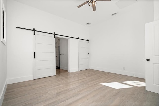 unfurnished bedroom with a barn door, ceiling fan, and light hardwood / wood-style floors