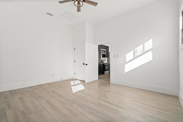 unfurnished room with a towering ceiling, light wood-type flooring, and ceiling fan