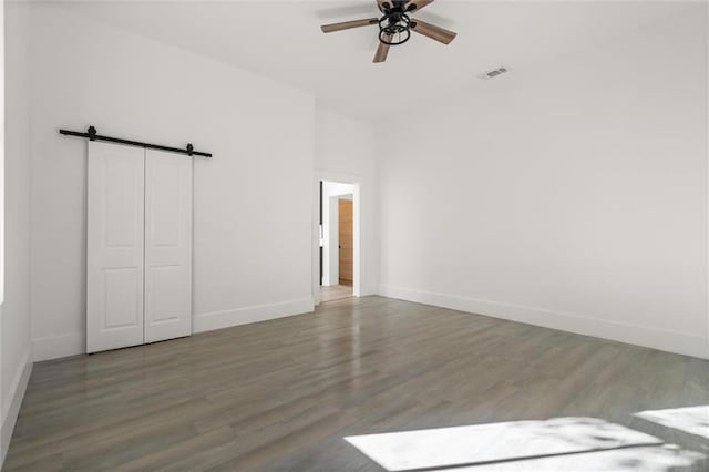 unfurnished bedroom featuring a closet, a barn door, hardwood / wood-style flooring, and ceiling fan