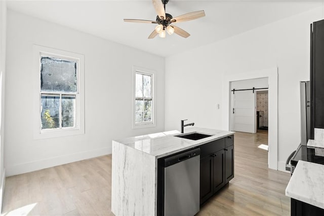 kitchen featuring sink, a barn door, stainless steel dishwasher, light hardwood / wood-style floors, and a center island with sink