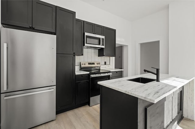 kitchen featuring backsplash, sink, light wood-type flooring, appliances with stainless steel finishes, and light stone counters