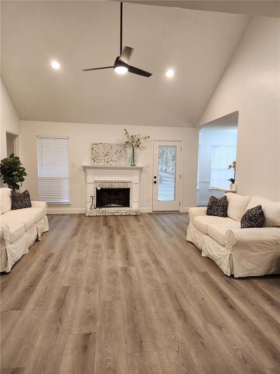 living area with baseboards, a fireplace with raised hearth, a ceiling fan, wood finished floors, and high vaulted ceiling