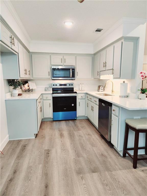 kitchen with sink, light wood-type flooring, ornamental molding, gray cabinets, and stainless steel appliances