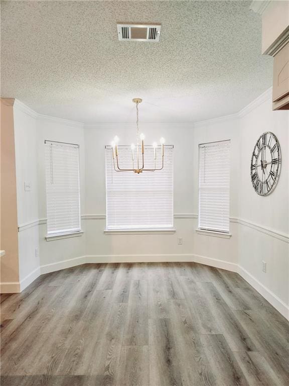 unfurnished dining area featuring crown molding, wood-type flooring, a textured ceiling, and an inviting chandelier