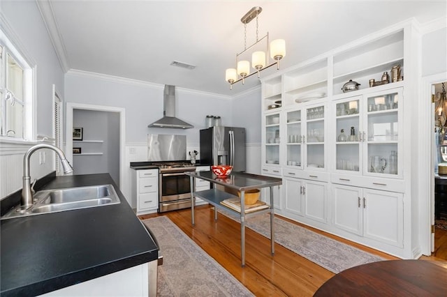 kitchen featuring visible vents, wall chimney exhaust hood, appliances with stainless steel finishes, white cabinetry, and a sink