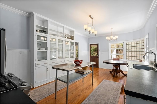 kitchen with white cabinets, a wainscoted wall, wood finished floors, an inviting chandelier, and a sink