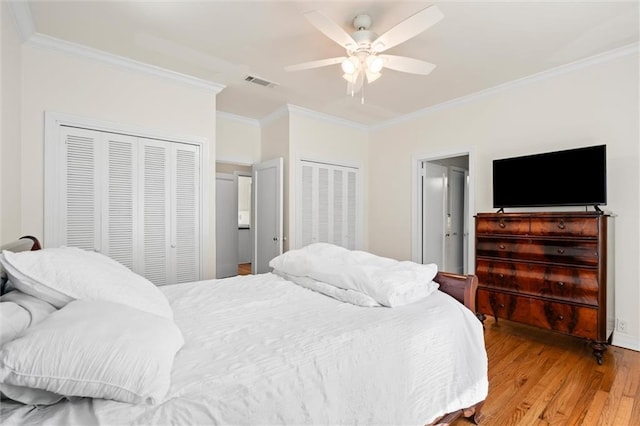 bedroom with light wood-type flooring, two closets, visible vents, and crown molding