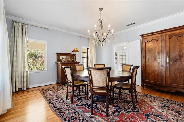 dining space featuring baseboards, visible vents, ornamental molding, an inviting chandelier, and light wood-type flooring