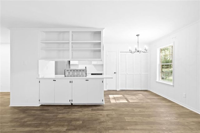 interior space with white cabinetry, an inviting chandelier, ornamental molding, pendant lighting, and dark wood-type flooring