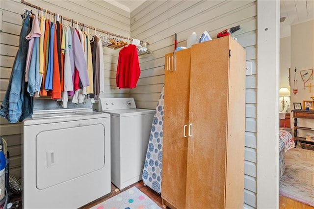 laundry room featuring laundry area, wooden walls, wood finished floors, and washing machine and clothes dryer