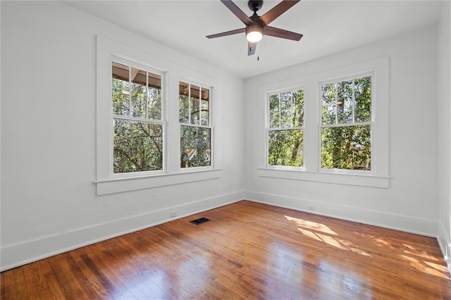 empty room featuring hardwood / wood-style floors, visible vents, baseboards, and ceiling fan