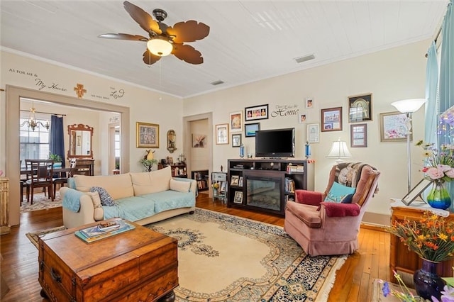 living room featuring visible vents, wood-type flooring, a ceiling fan, and crown molding