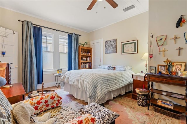 bedroom with a ceiling fan, baseboards, wood finished floors, visible vents, and ornamental molding