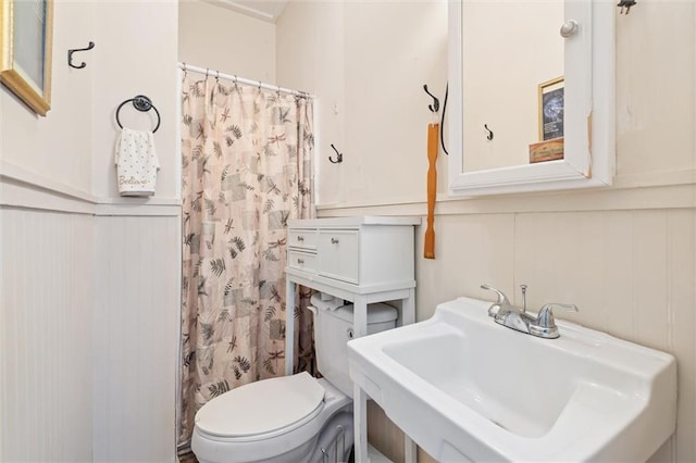 full bath with a shower with curtain, toilet, a wainscoted wall, and a sink