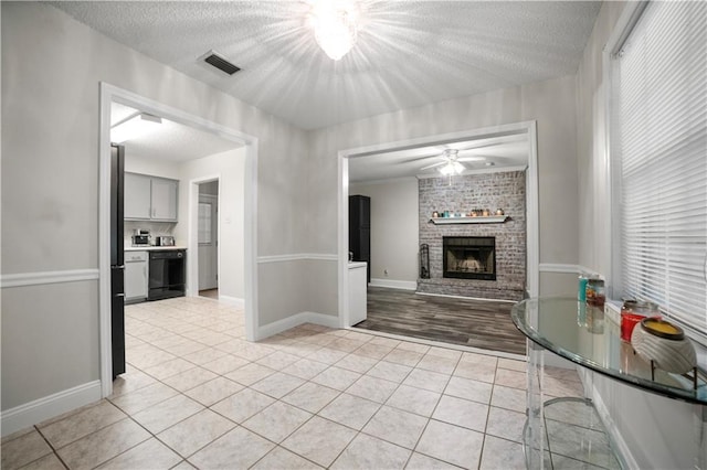 unfurnished living room with ceiling fan, a textured ceiling, a brick fireplace, and light tile patterned floors