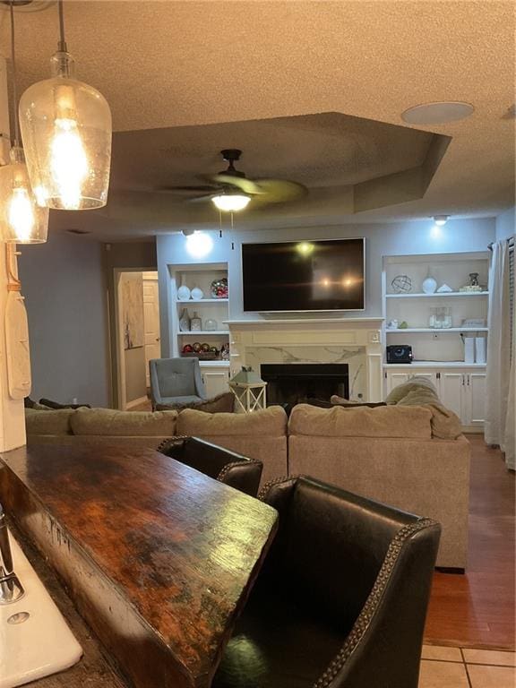 living room featuring a premium fireplace, built in features, ceiling fan, and a textured ceiling