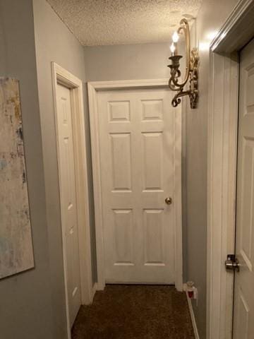 hall featuring dark carpet and a textured ceiling