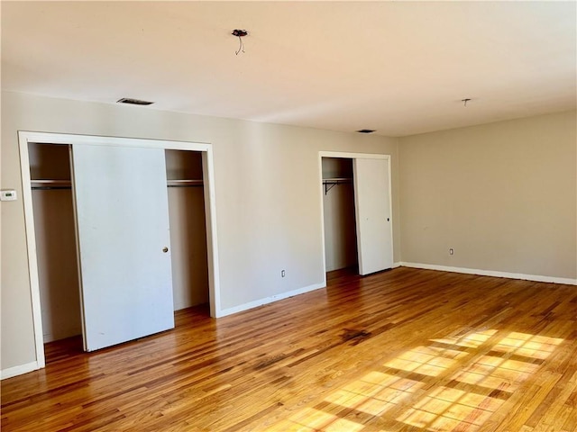 unfurnished bedroom with multiple closets, visible vents, light wood-style flooring, and baseboards