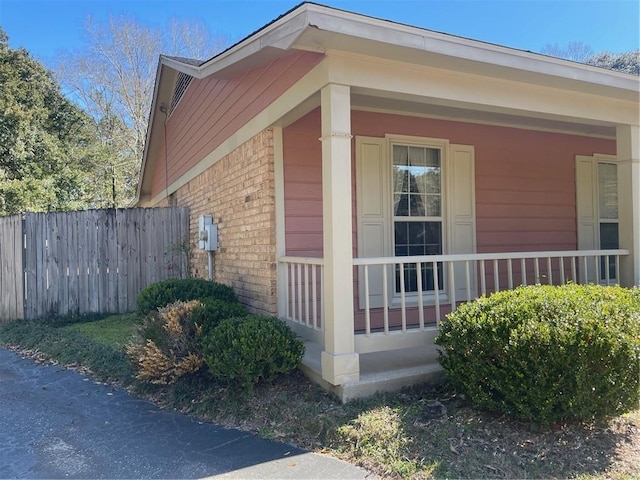 view of property exterior with a porch, brick siding, and fence