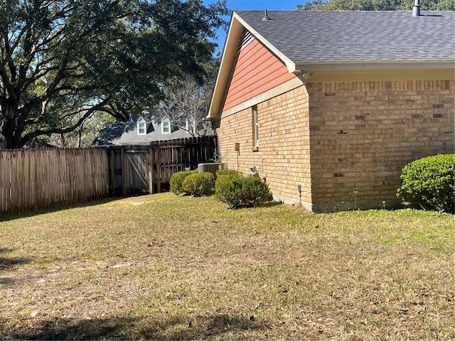 view of side of home with a shingled roof, brick siding, fence, and a lawn