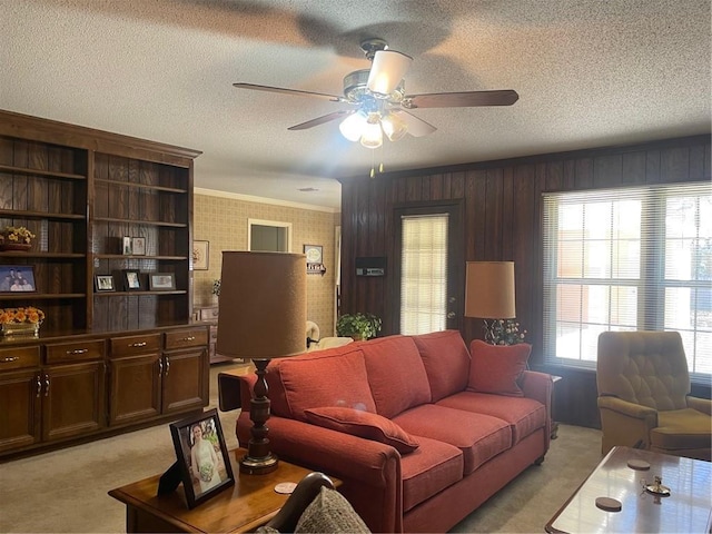 living area with a ceiling fan, light colored carpet, crown molding, and a textured ceiling