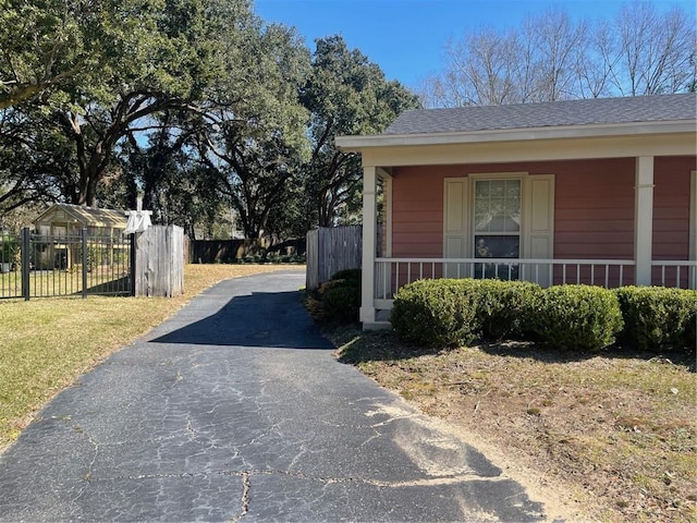 view of side of property featuring a yard, a porch, a shingled roof, fence, and driveway