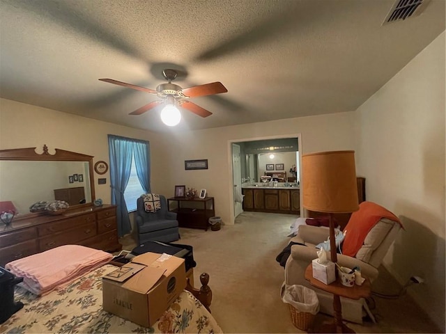 bedroom featuring light carpet, visible vents, a ceiling fan, ensuite bathroom, and a textured ceiling