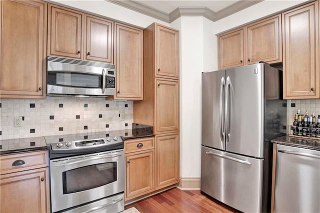 kitchen with dark stone countertops, appliances with stainless steel finishes, tasteful backsplash, and wood-type flooring