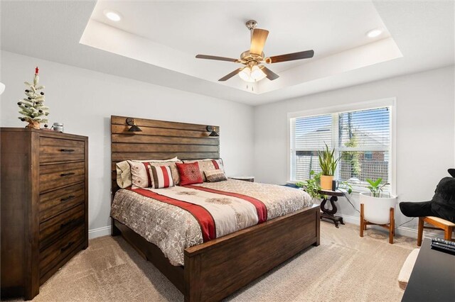 bedroom featuring a raised ceiling, baseboards, and light carpet