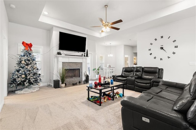 carpeted living area with a fireplace with flush hearth, a tray ceiling, recessed lighting, baseboards, and ceiling fan