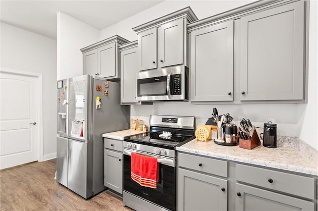 kitchen with light stone counters, light wood finished floors, appliances with stainless steel finishes, and gray cabinetry